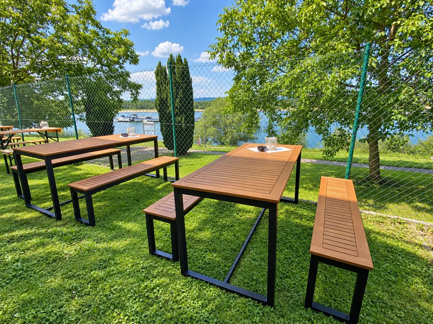 Holztische auf der Wiese im hinteren Biergarten, dahinter der Rhein